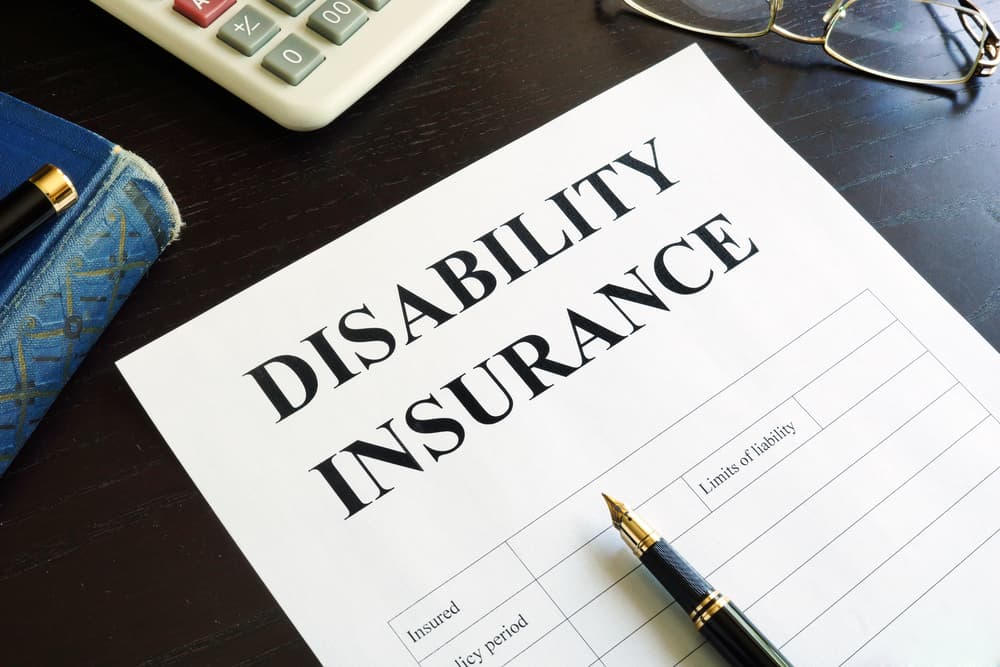 On the table lies a disability insurance form alongside a pen and a calculator, indicating the process of assessing and managing disability coverage.