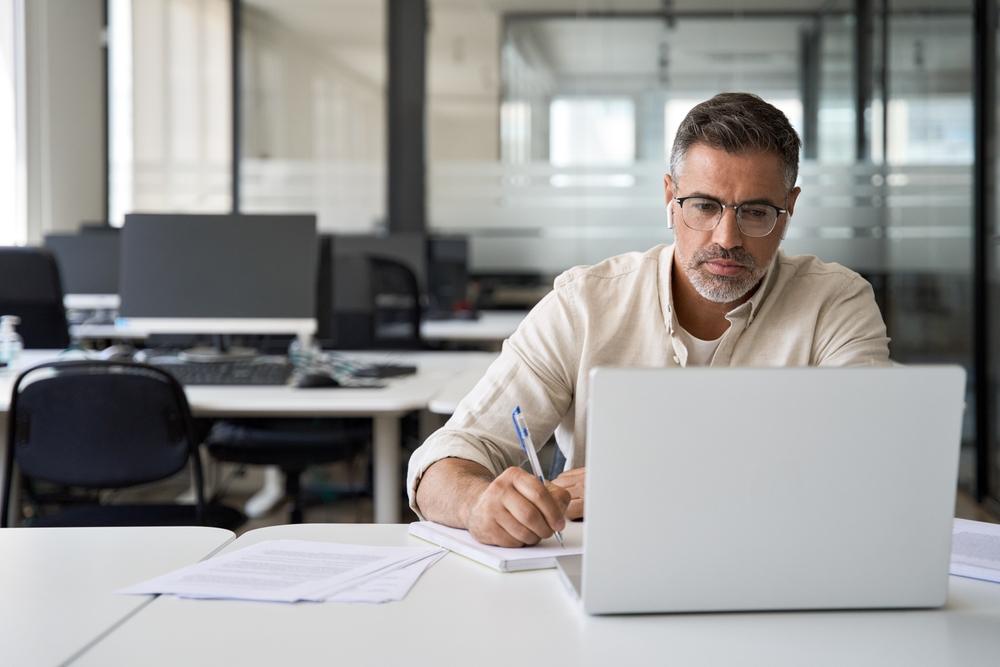 A middle-aged man researches on his laptop at work the difference between life insurance conversion and portability.