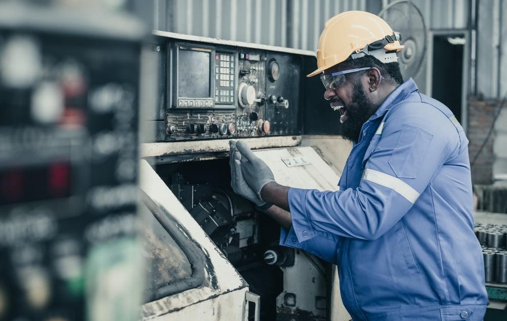 Factory worker reacting in pain while holding his hand beside industrial machinery